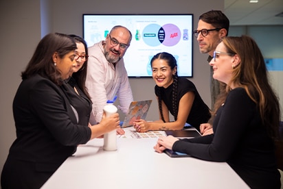Six Colgate-Palmolive employees in a meeting room discussing a product concept, with a presentation slide on a screen behind them.
