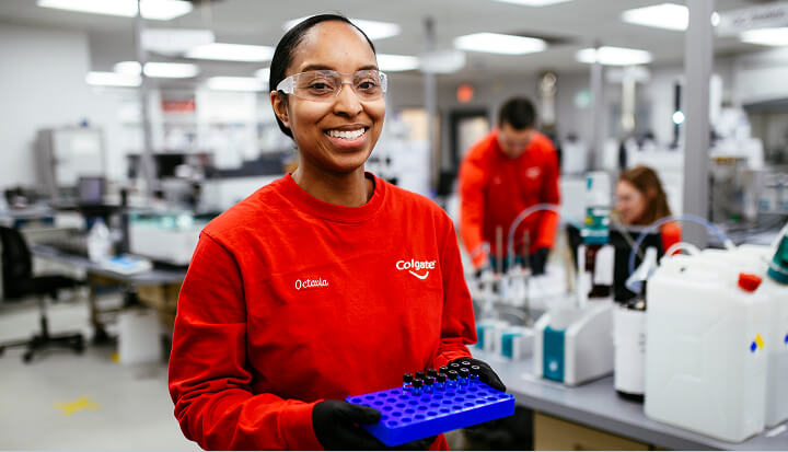 Colgate scientist in red shirt and safety glasses working with laboratory equipment.